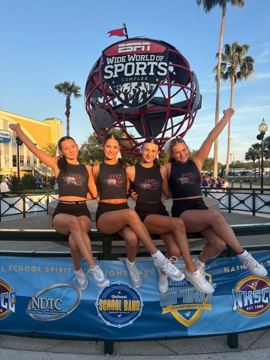 Four Westosha Central cheerleaders sitting in front of the ESPN Wide World of Sports globe